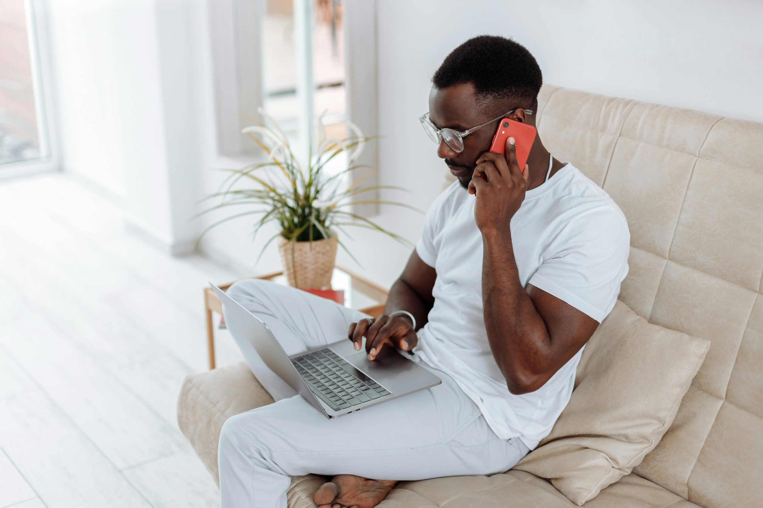 a male on the phone with laptop while sitting on the couch