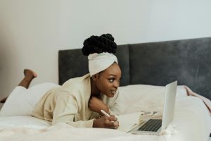A Woman Taking Notes while Reading on a Laptop