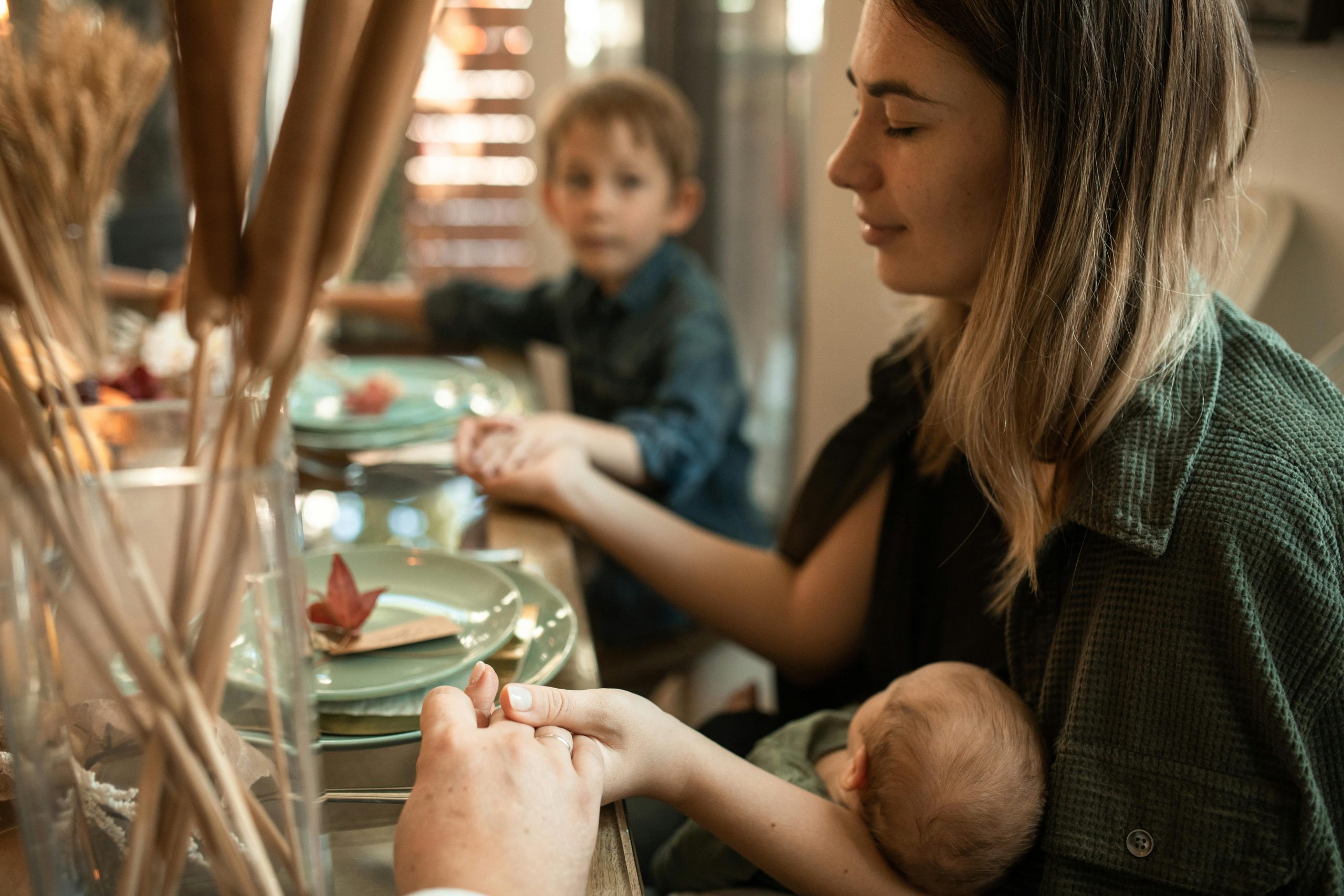 woman at table holding baby and praying with children