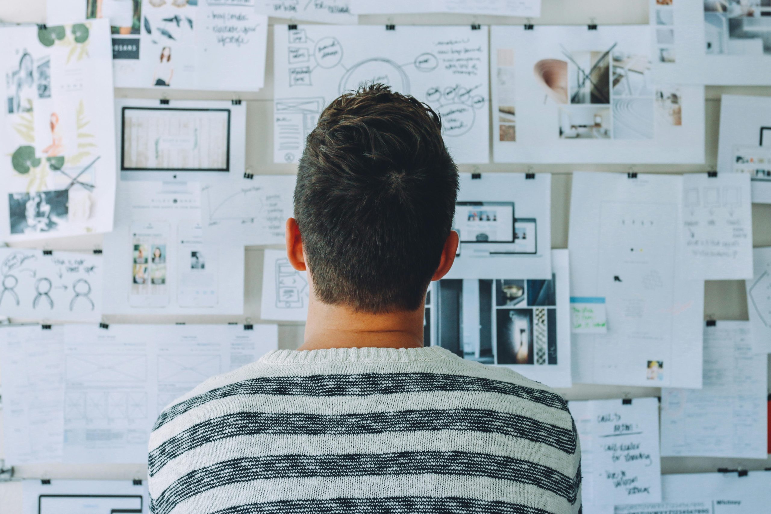 man staring at bulletin board full of notes and pictures
